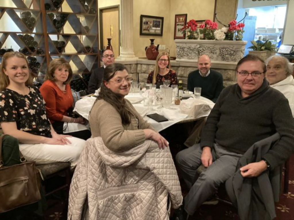 A photo of Maddie and various members of The Wandering Francophones, sitting at a table at an Italian restaurant.