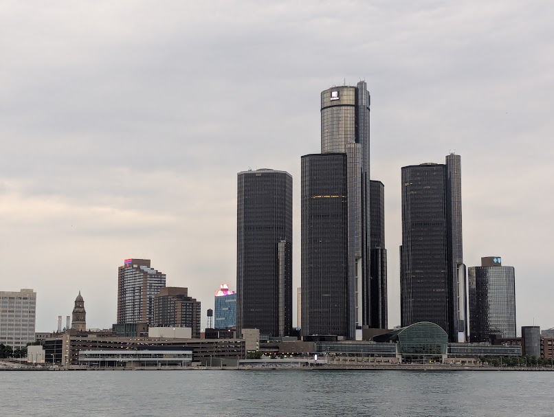 An image of downtown Detroit, notably its skyscrapers surrounding the GM Renaissance building, with a cloudy overcast sky in the background