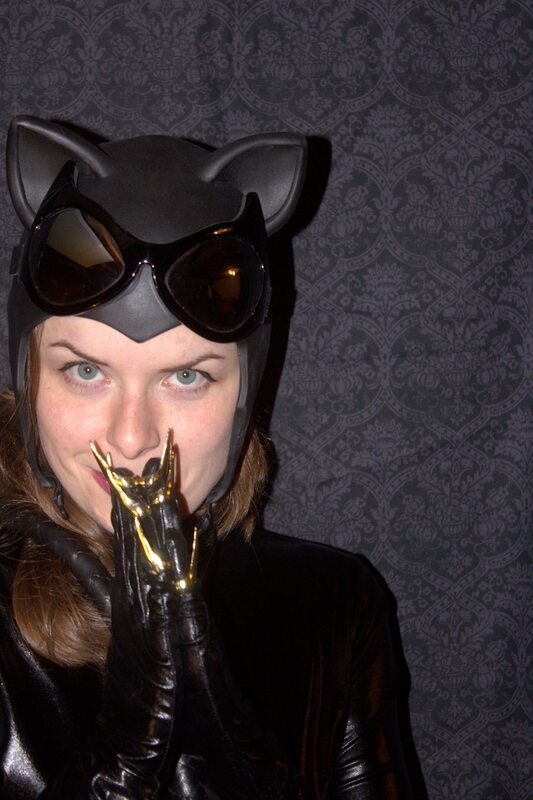 A close up image of Maddie in a black Catwoman hat with cat-like glasses sitting atop her head, wearing black gloves with gold nails attached to them.