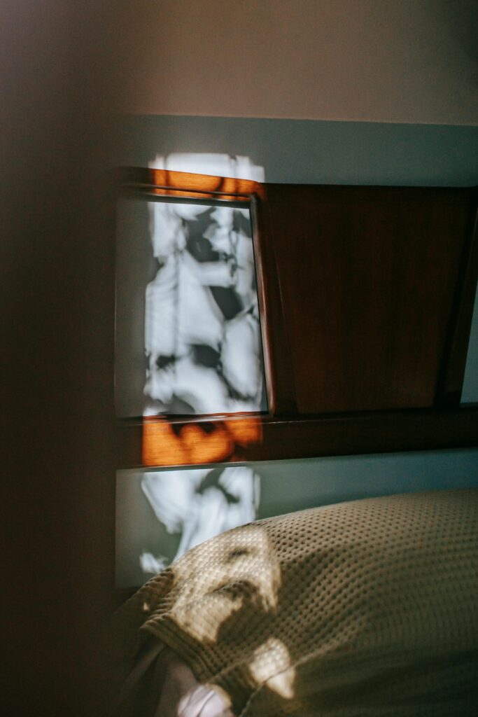 A photo of a dark bedroom with a tree casting its leafy shadow on the wall.