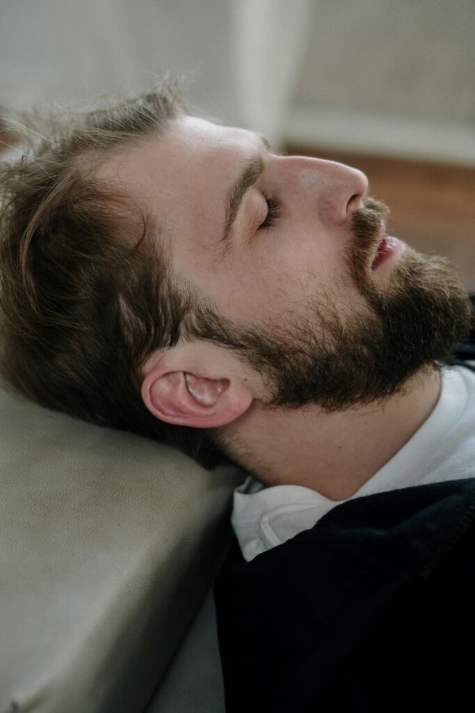 A bearded man lying down with this eyes closed.