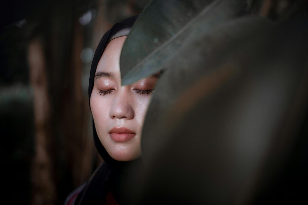 A person with their eyes closed behind large green leaves