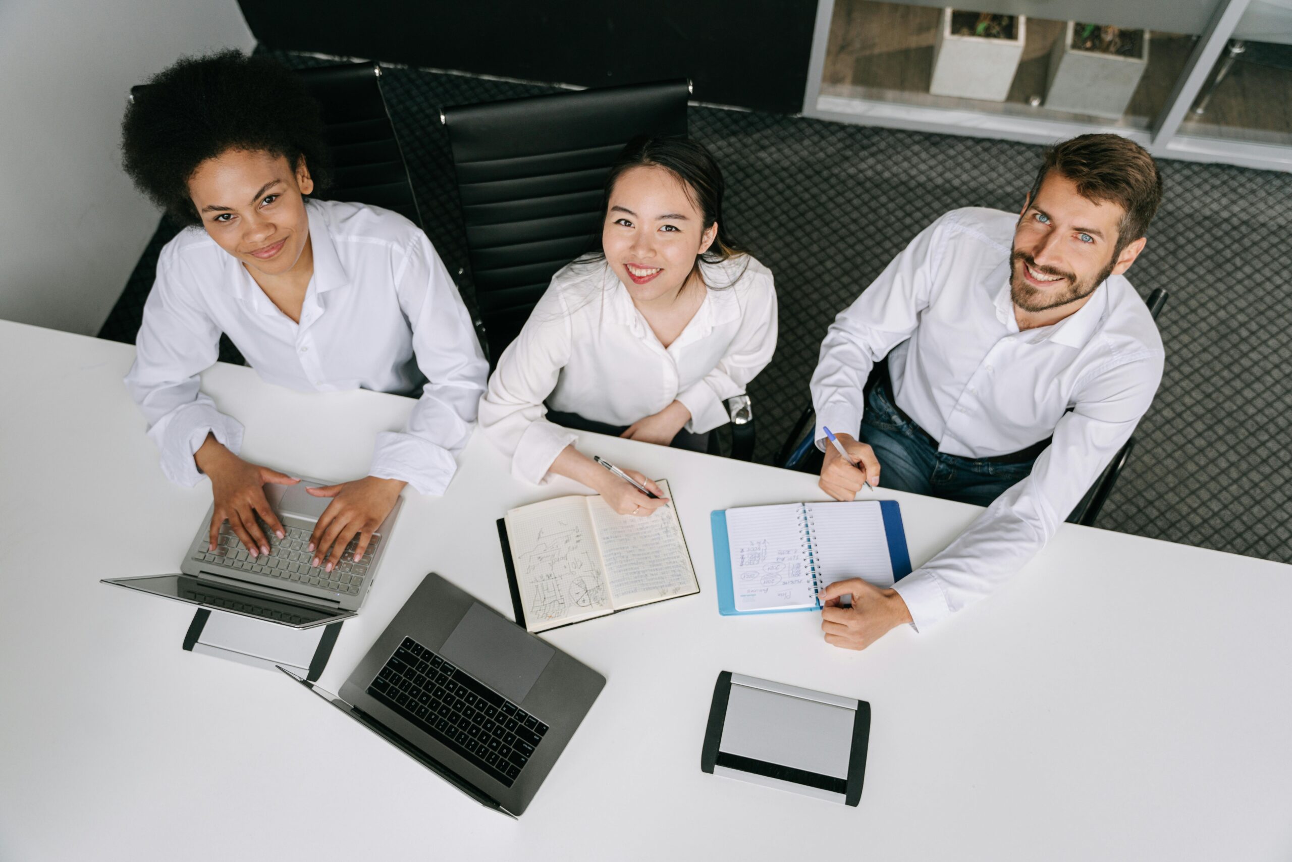 A stock image of three professionals sitting at a desk with white shirts, looking up at the camera taking an aerial picture of them.