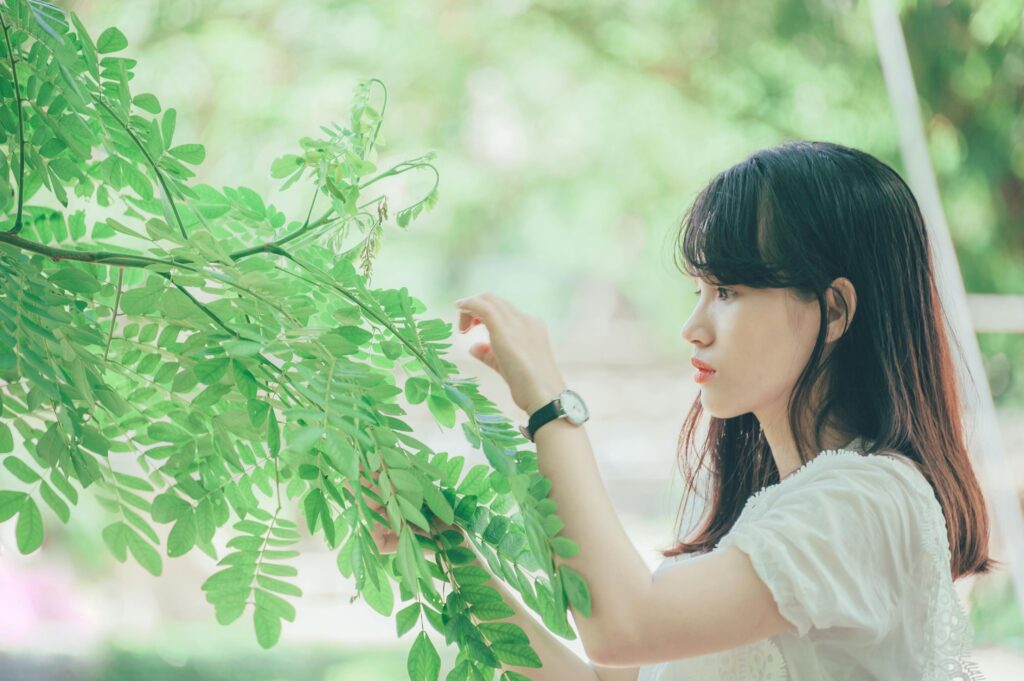 A woman with a watch looking closely at a tree branch with many green leaves.