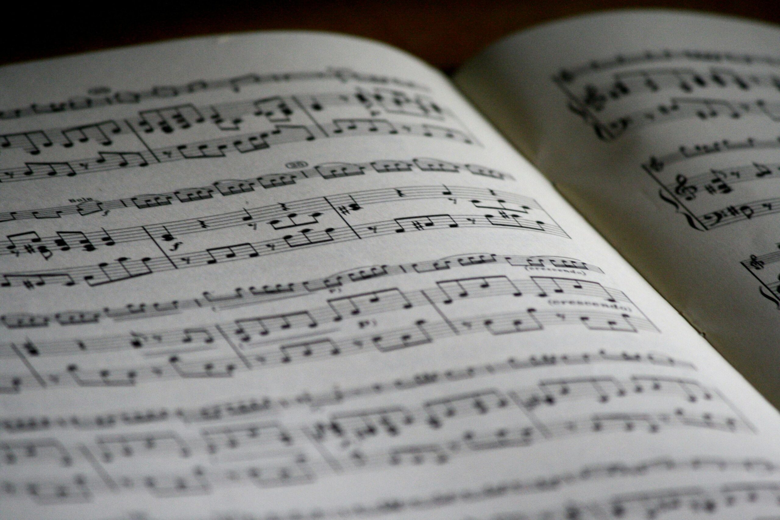 A close up photo of a music book opened to a page with many musical notes with a dark background.