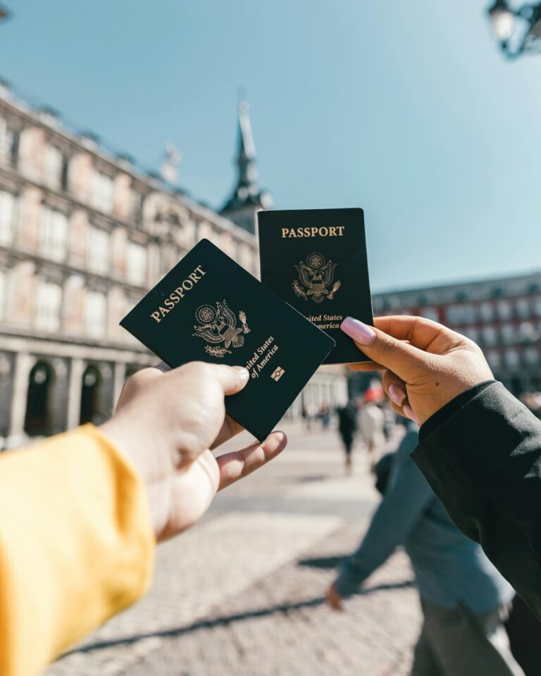 Two hands holding blue US passports up against a background of a building.