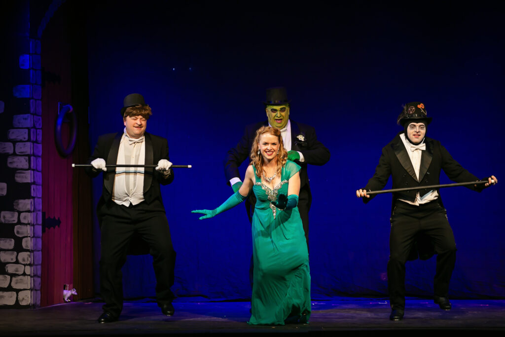 A photo of the theatrical production of Young Frankenstein, with Alex as Frederick holding a cane, next to the Monster (played by Jared) and Igor (played by Dylan), tapping in black and white tuxedoes with Maddie as Inga in a teal dress tapping in front of them.