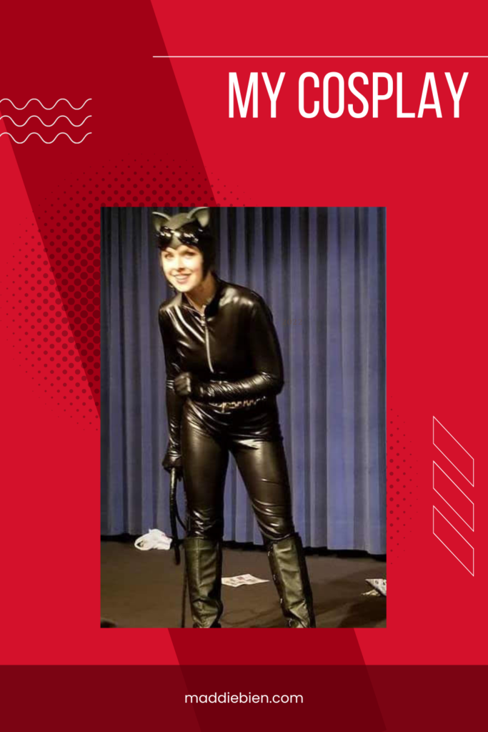 An image of Maddie dressed in a Catwoman costume with a red background, holding a whip in her right hand, with blue stage curtains behind her and various papers strewn about the floor.